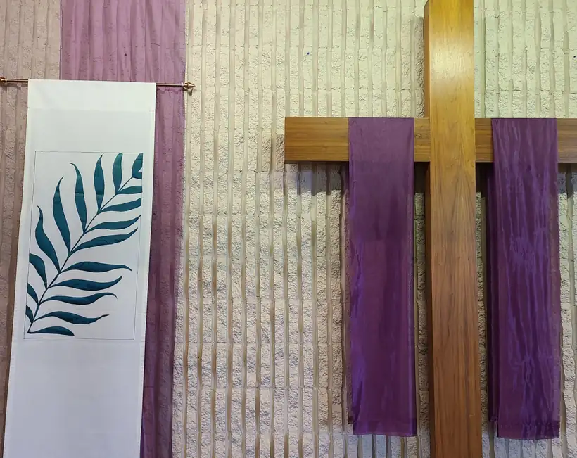 Palm banner and a wooden cross draped in purple on the ribbed sanctuary wall at Bethel.