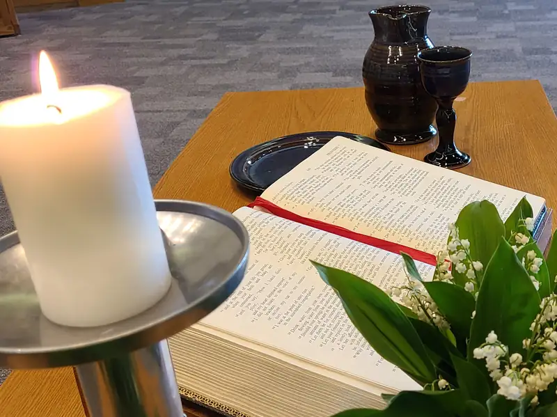 Bethel's communion table: an open Bible, a lit pillar candle, slate-glazed pottery and lily of the valley on honey-toned oak.
